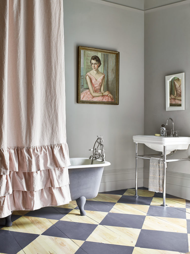 A wood and dark grey chequerboard floor in this grey painted bathroom adds a modern twist and the pink shower curtain softens the scheme.