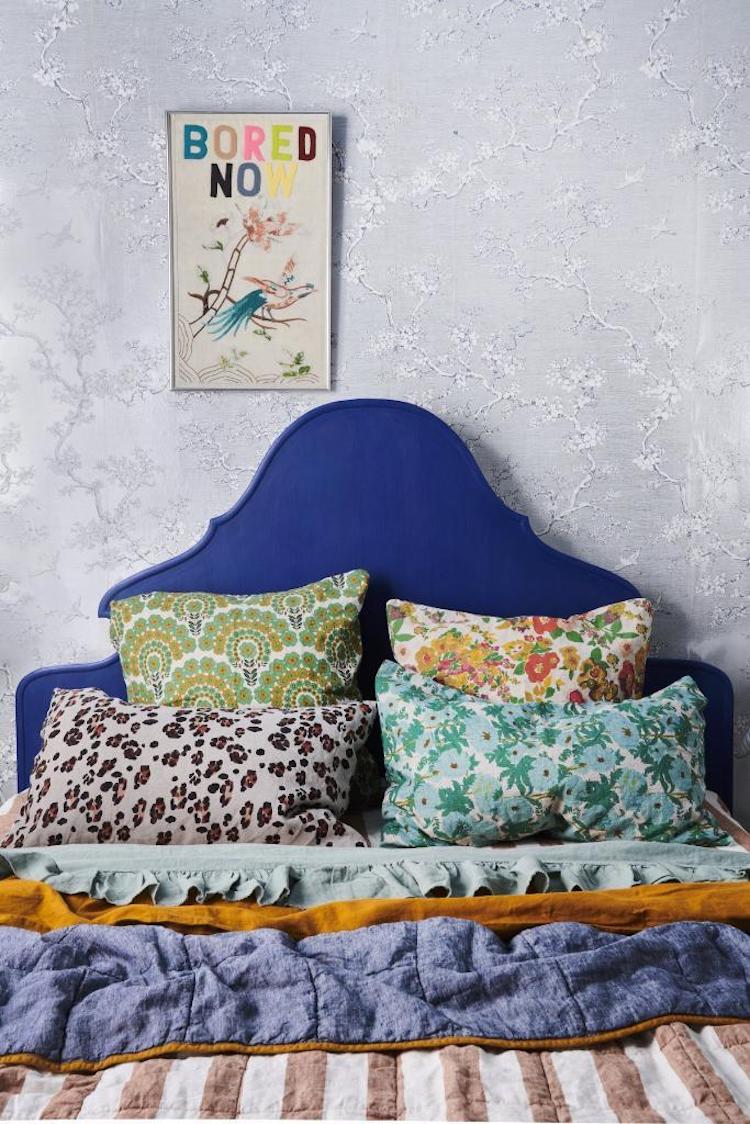 Mixture of patterned cushions on a bed with linen covers and cobalt blue headboard, bedding by society of wanderers