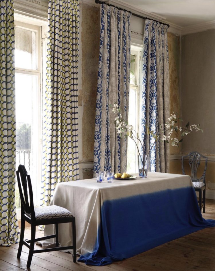 two pairs of curtains in one room, both blue pattern with a bold blue and linen tablecloth. styling by sarita sharma for clarke and clarke