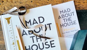 Mad About the House, new book scattered with stationery and tape measure on wooden table.