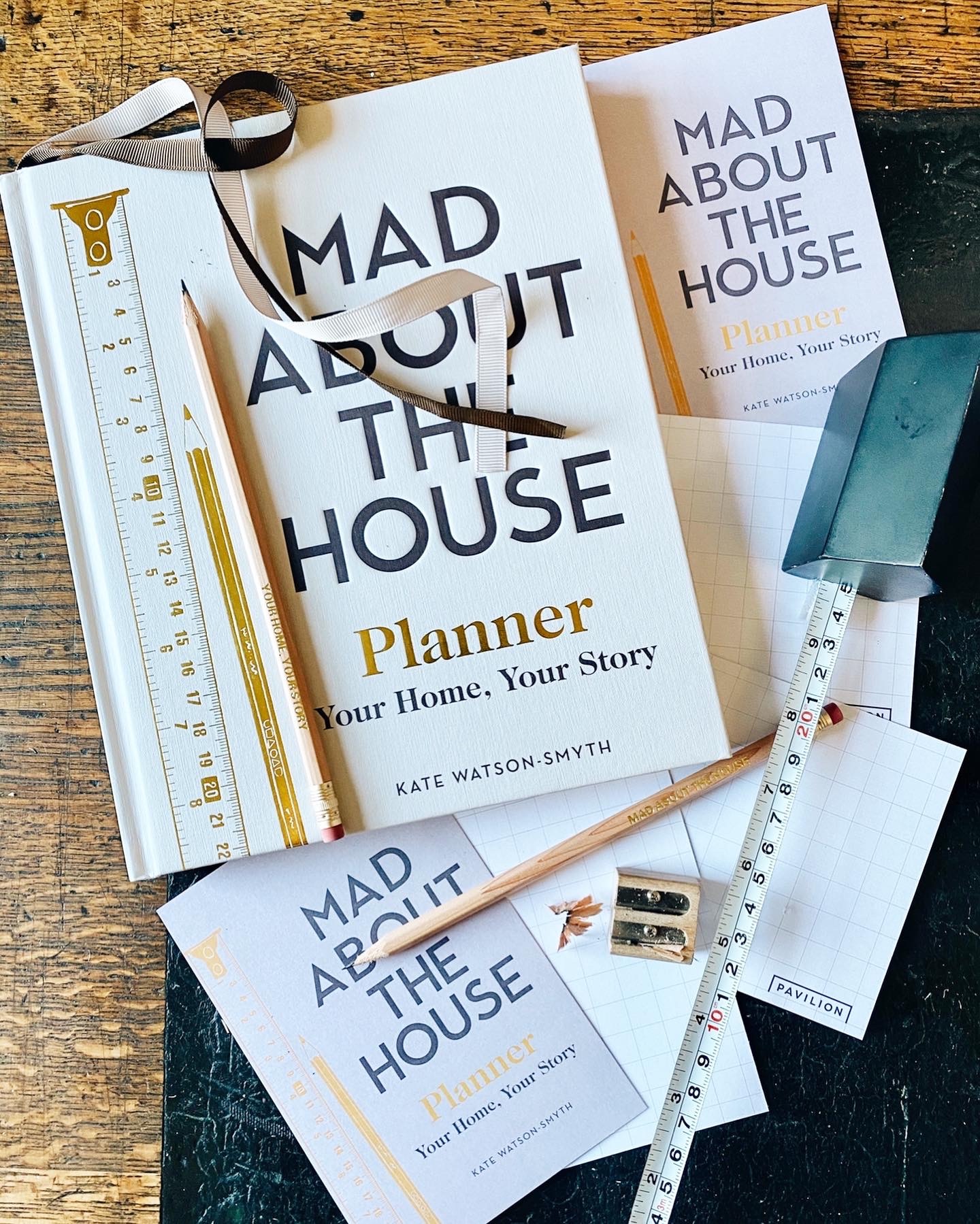 Mad About the House, new book scattered with stationery and tape measure on wooden table.
