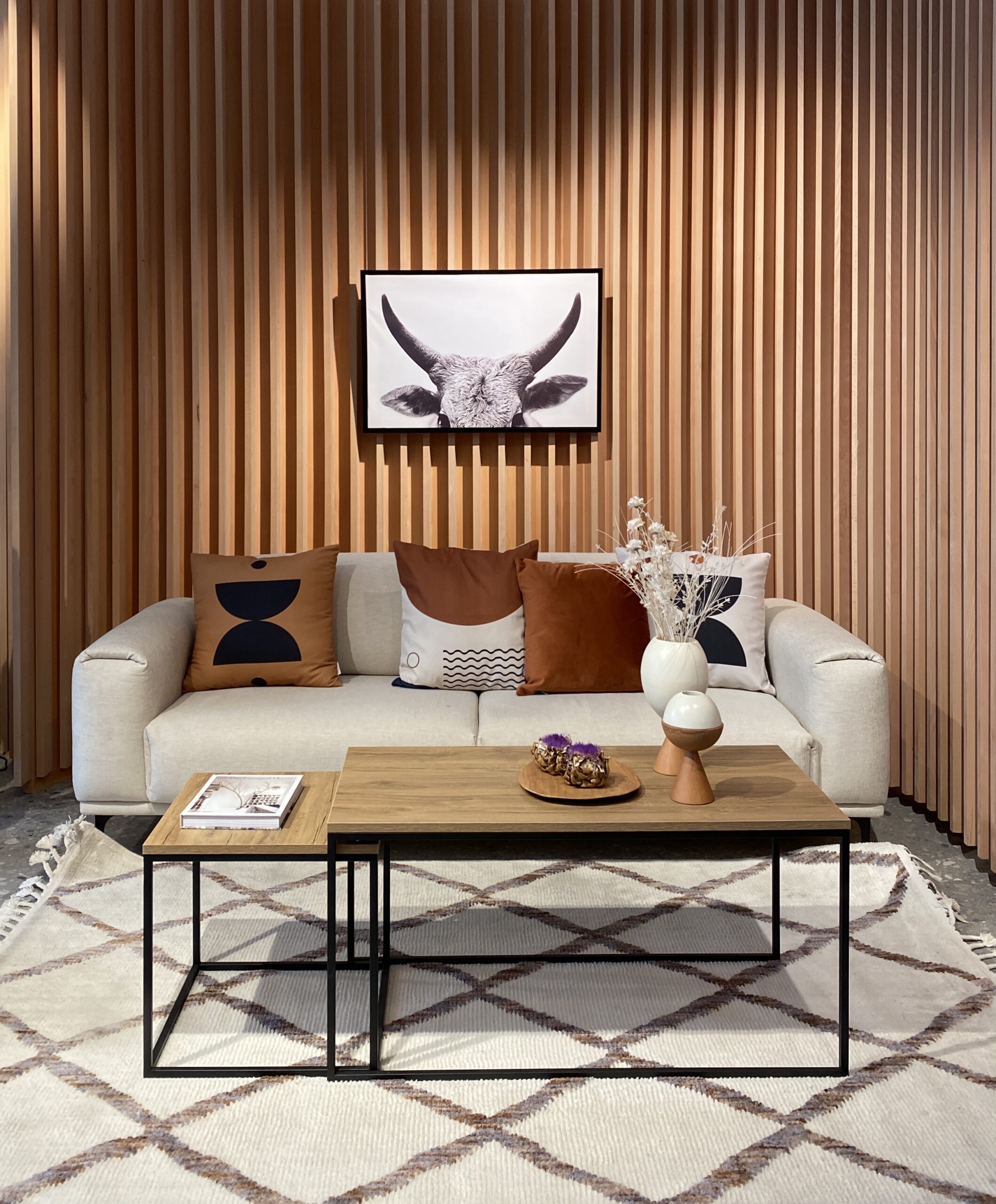 Curved fluted panelled wooden walls, cream modern sofa, black frame and wooden coffee tables, Berber style rug from vivense